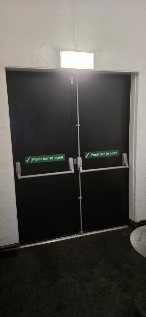 Inside face of steel double doors with push bars and emergency exit signage