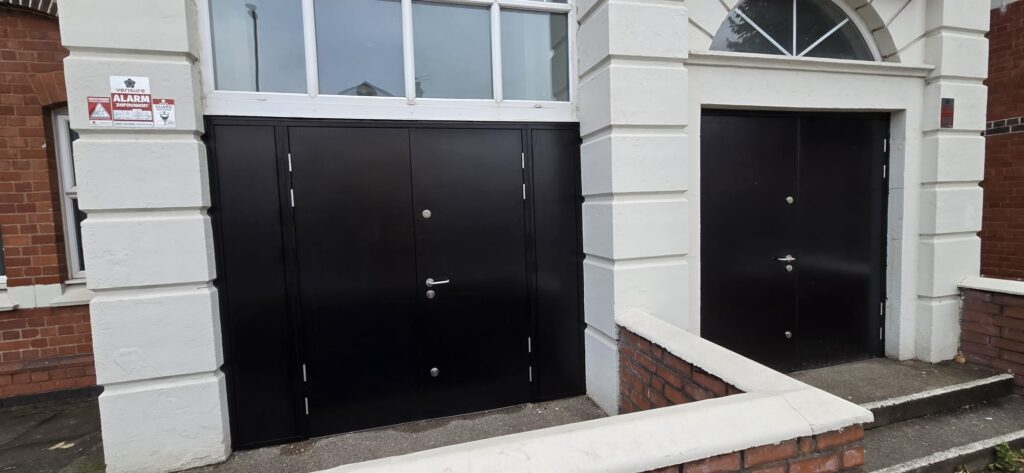Two black steel security doorsets on the rendered front entrance of a Coventry church