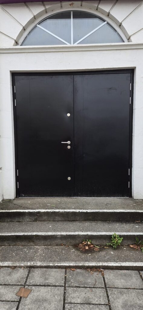 Black steel double doors with stainless lever handle beneath an arched fanlight, church main entrance