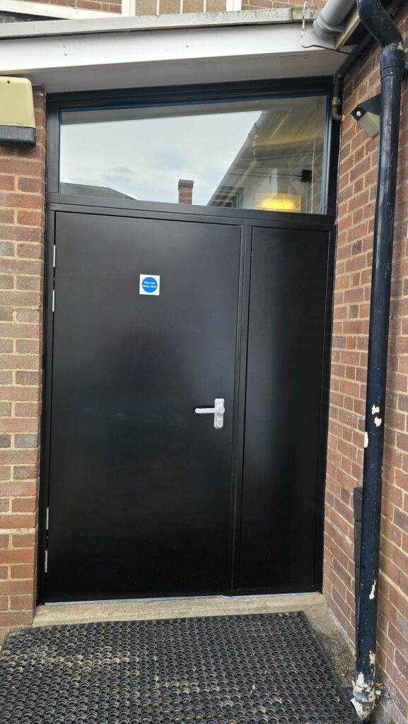 Single steel fire exit door with blanking side panel and angled glazing unit above, Marpe Centre Coventry